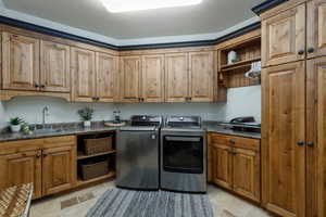 Laundry room featuring extensive wood cabinetry with dark hardware, a built-in sink with a gooseneck faucet, ample counter space, and open shelving