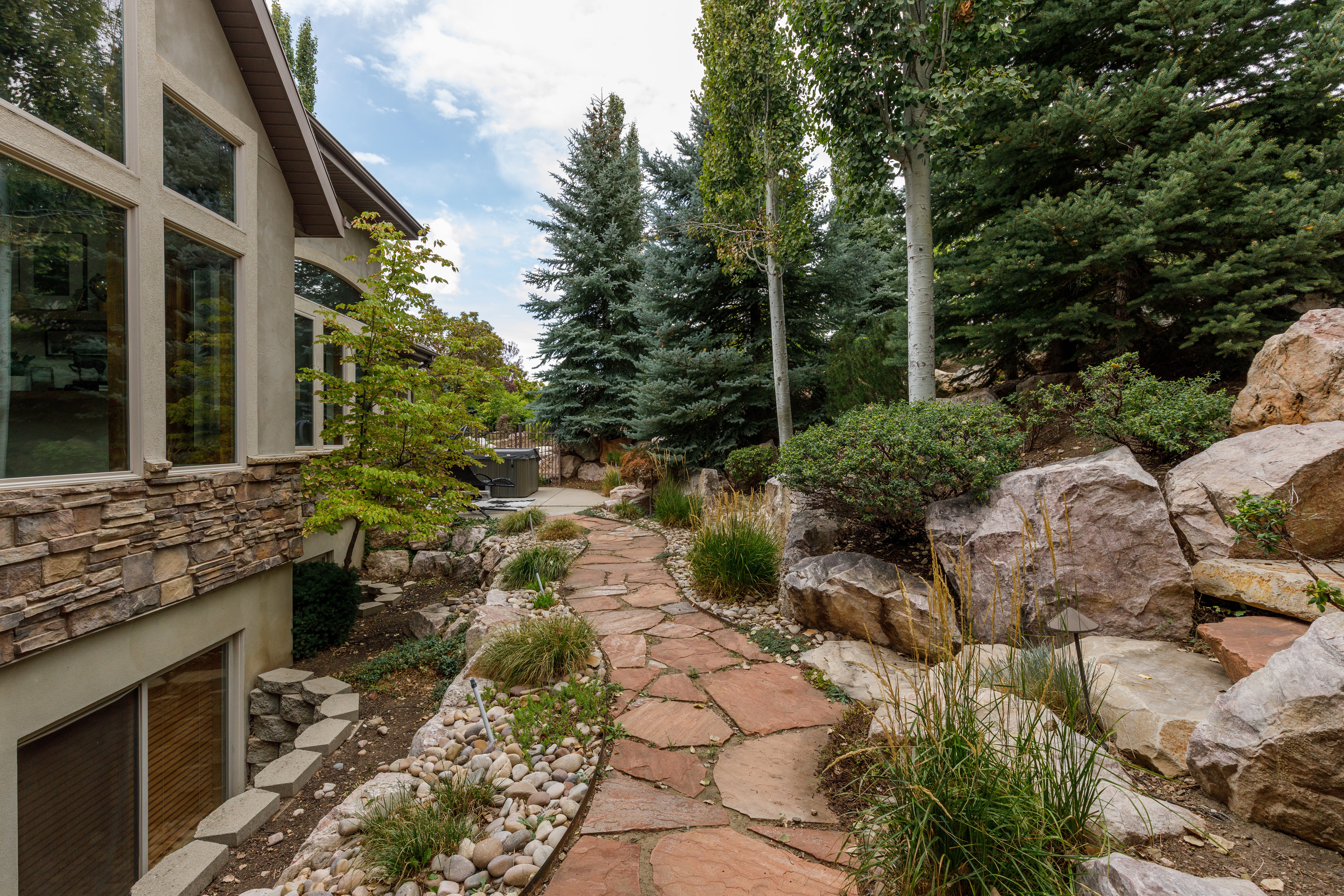 Flagstone pathway bordered by decorative river rock and boulders, leading to a built-in hot tub
