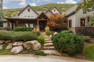 Stone and stucco exterior featuring wood-finish shutters, a covered entry porch with exposed beams, and a natural stone walkway