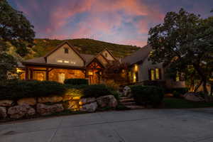 Stone and stucco exterior with exposed timber architectural accents, a multi-gabled roofline, and established landscaping featuring mature trees and rock retaining walls