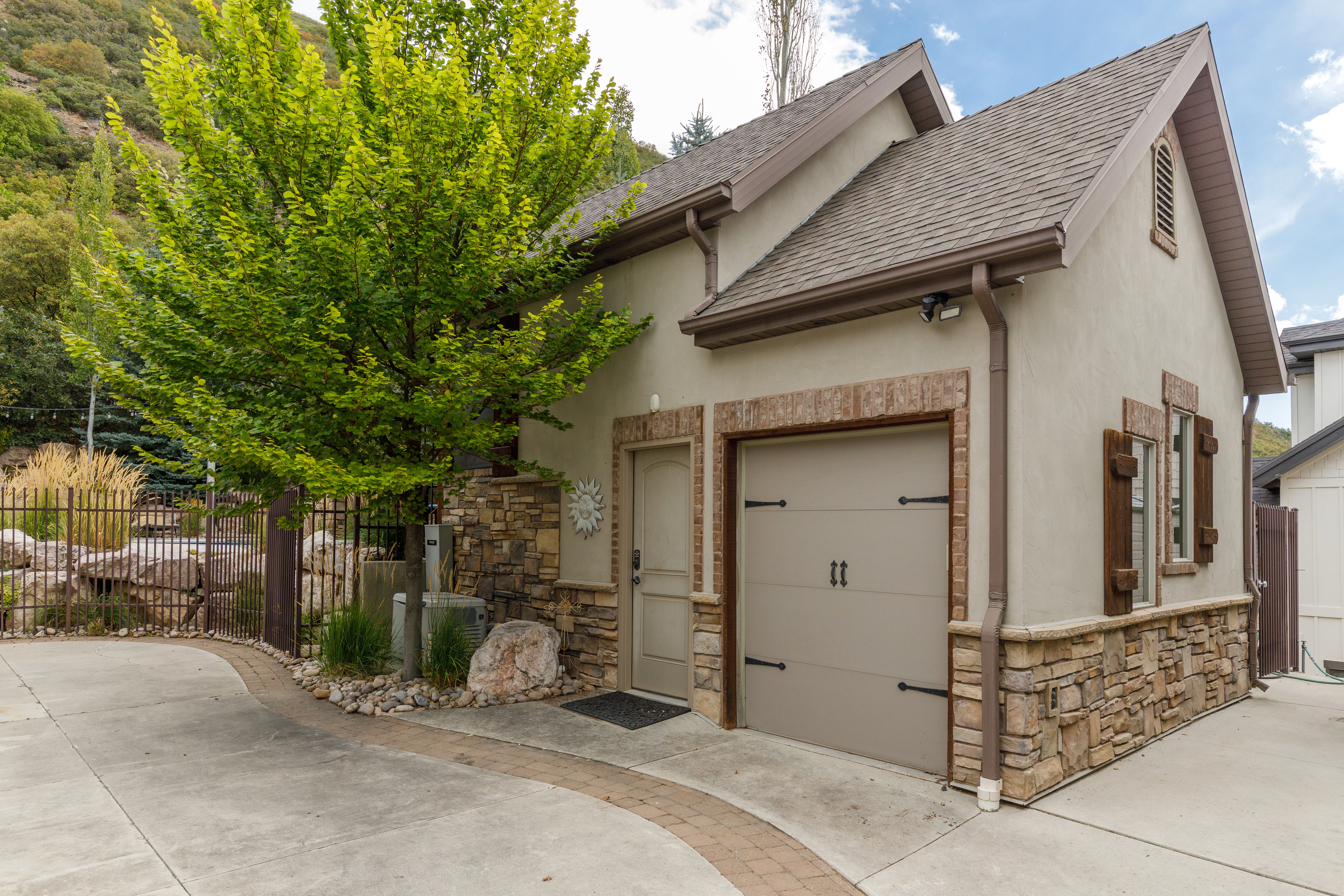 Detached structure featuring a stucco exterior with stone accents, a single garage door with decorative hardware, and two windows with rustic shutters