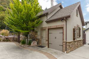 Detached structure featuring a stucco exterior with stone accents, a single garage door with decorative hardware, and two windows with rustic shutters