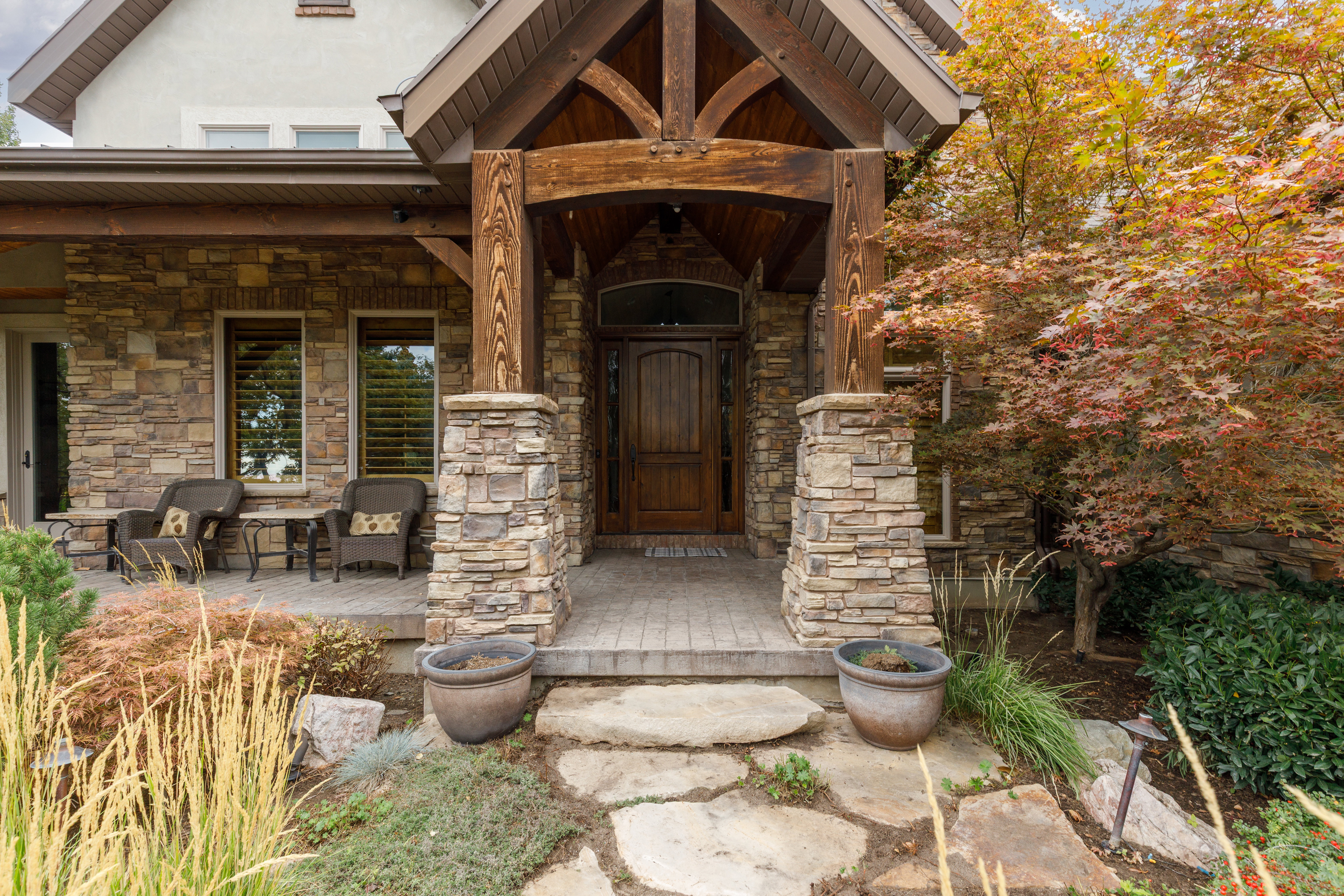 Stone veneer exterior with a prominent timber-frame entry, wood-paneled door, paver walkway, and a flagstone path