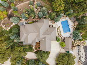 Sprawling property featuring a multi-gabled roofline, a rectangular swimming pool with surrounding patio, extensive landscaping with mature trees and stone pathways, a paved driveway, and an additional detached structure