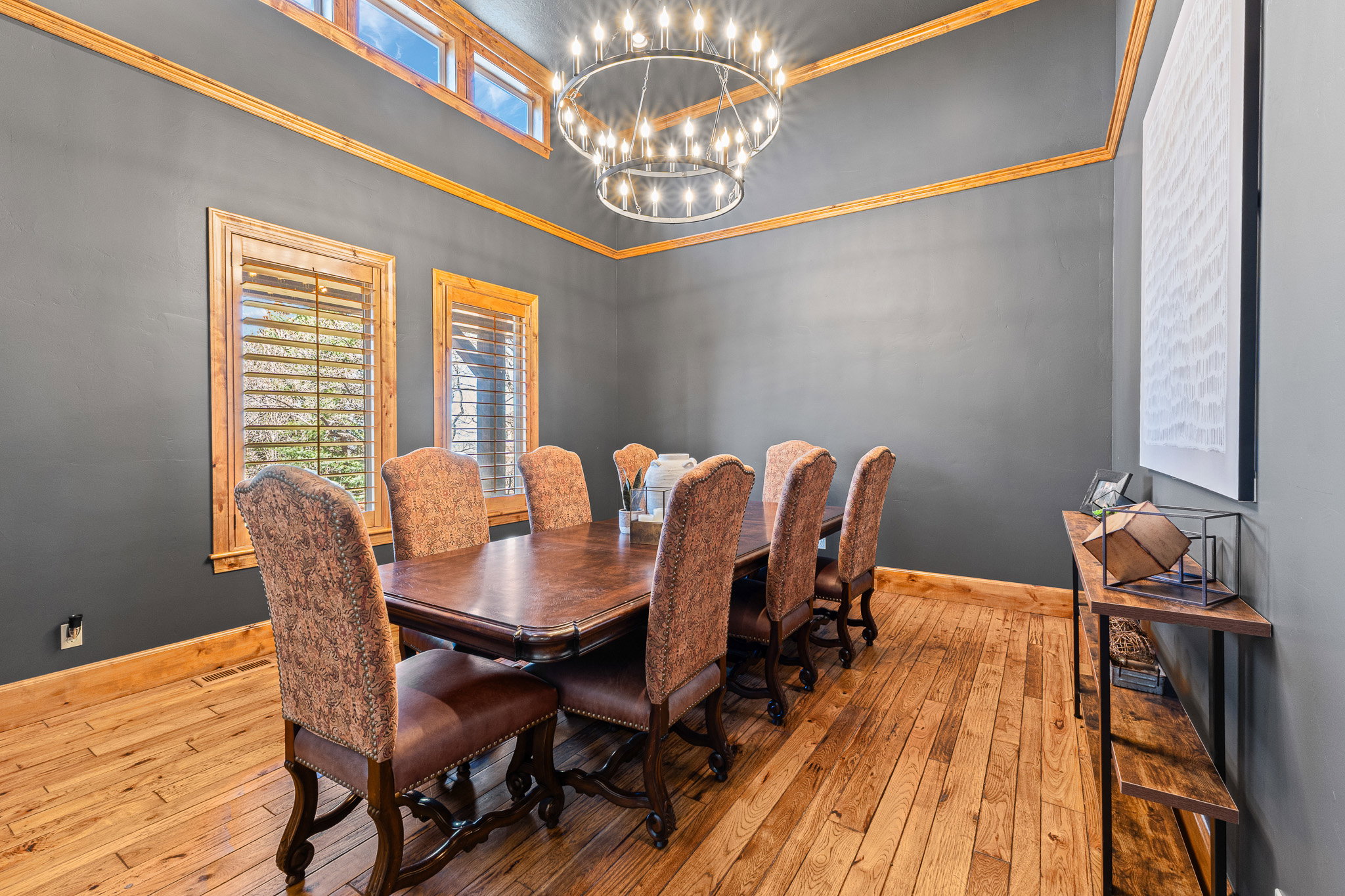 Dining area featuring high ceilings, wood-finish flooring, a tiered chandelier, transom windows, and dark wall finishes