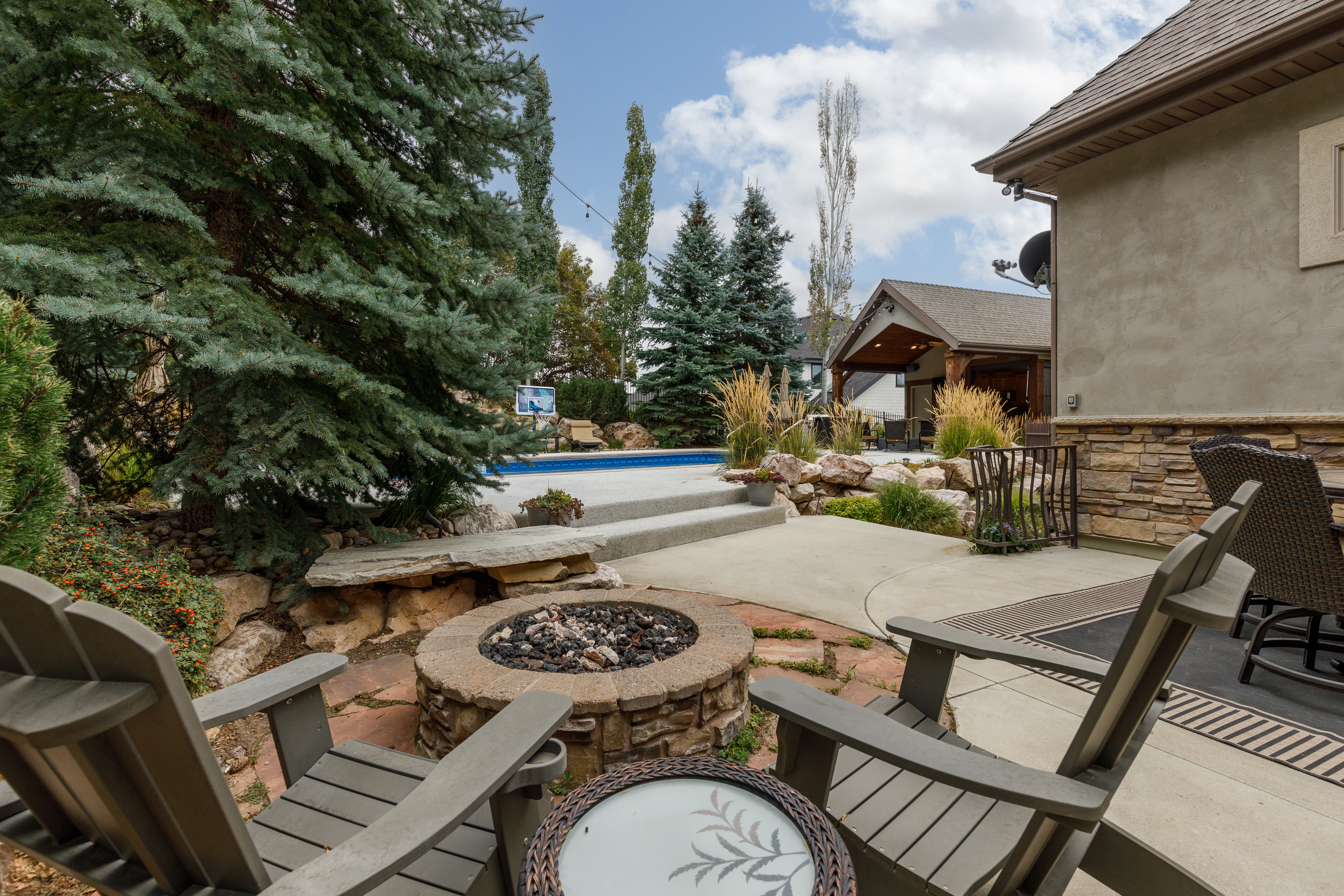 Backyard patio featuring a stone fire pit, concrete and flagstone paving, and a built-in swimming pool