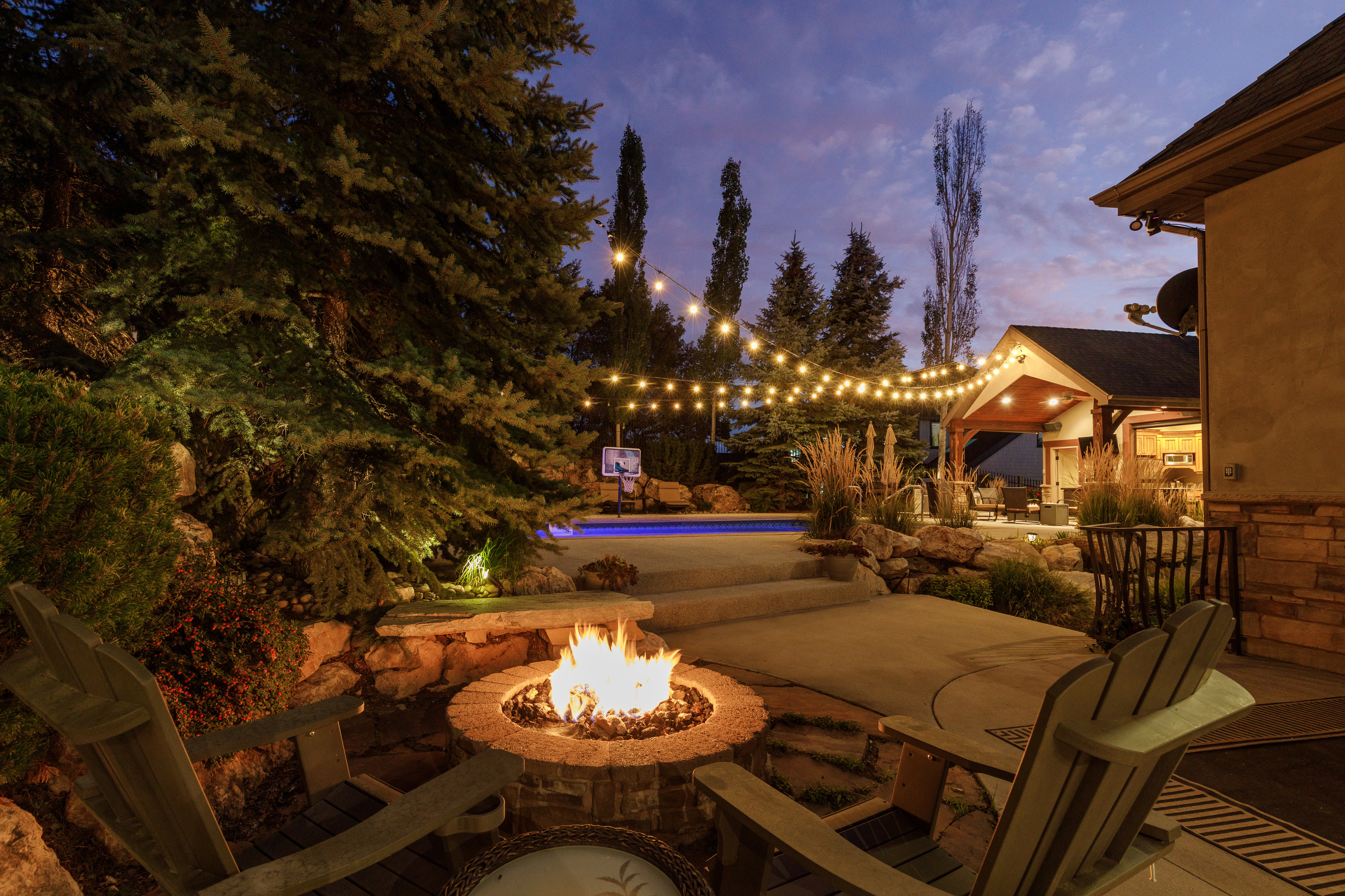 Outdoor living area featuring a stone fire pit, string lighting, and an in-ground pool
