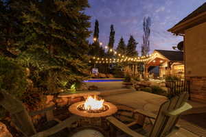 Outdoor living area featuring a stone fire pit, string lighting, and an in-ground pool