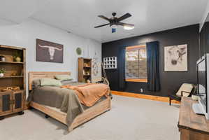 Carpeted bedroom featuring a dark accent wall, a window with blinds and drapes, a ceiling fan with integrated lighting, and wood-finish baseboards