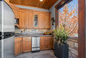 Kitchenette featuring wood cabinetry with glass-front accents, stainless steel appliances, and a wood-paneled ceiling