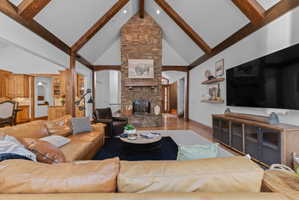 Living space featuring a vaulted ceiling with exposed wood beams, a stone fireplace, light wood-finish flooring, and built-in shelving