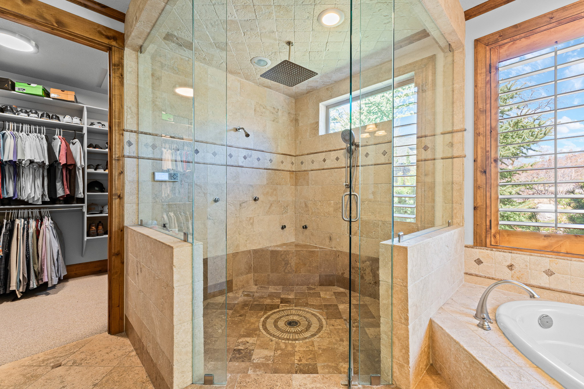 Spacious bathroom featuring a glass-enclosed shower with multiple shower heads and a rain shower fixture, an integrated shower bench, and tile flooring with a decorative mosaic inlay