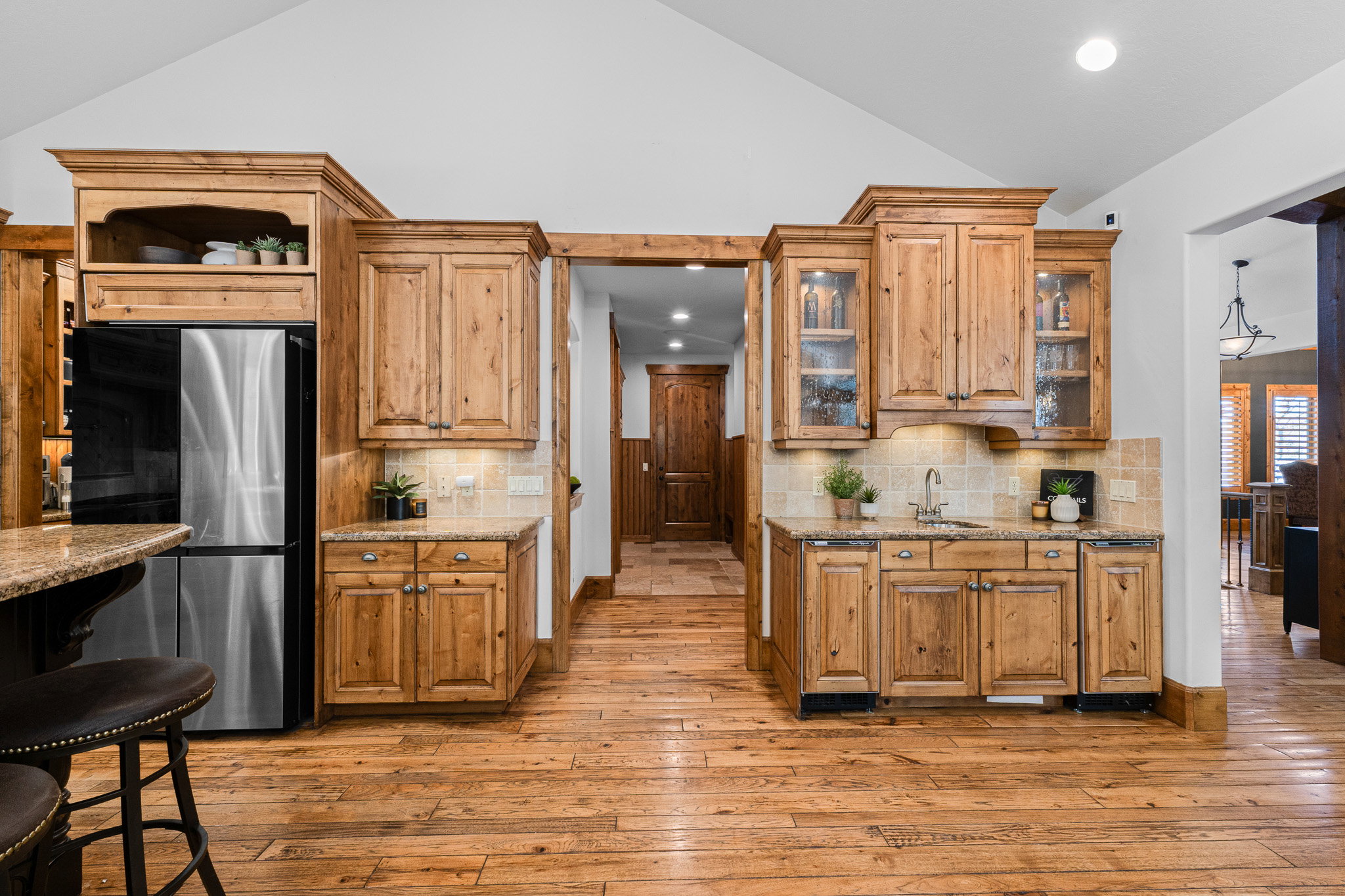 Vaulted ceiling kitchen featuring knotty wood cabinetry, stainless steel refrigerator, granite countertops, tile backsplash, and wood-finish flooring