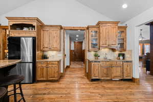 Vaulted ceiling kitchen featuring knotty wood cabinetry, stainless steel refrigerator, granite countertops, tile backsplash, and wood-finish flooring