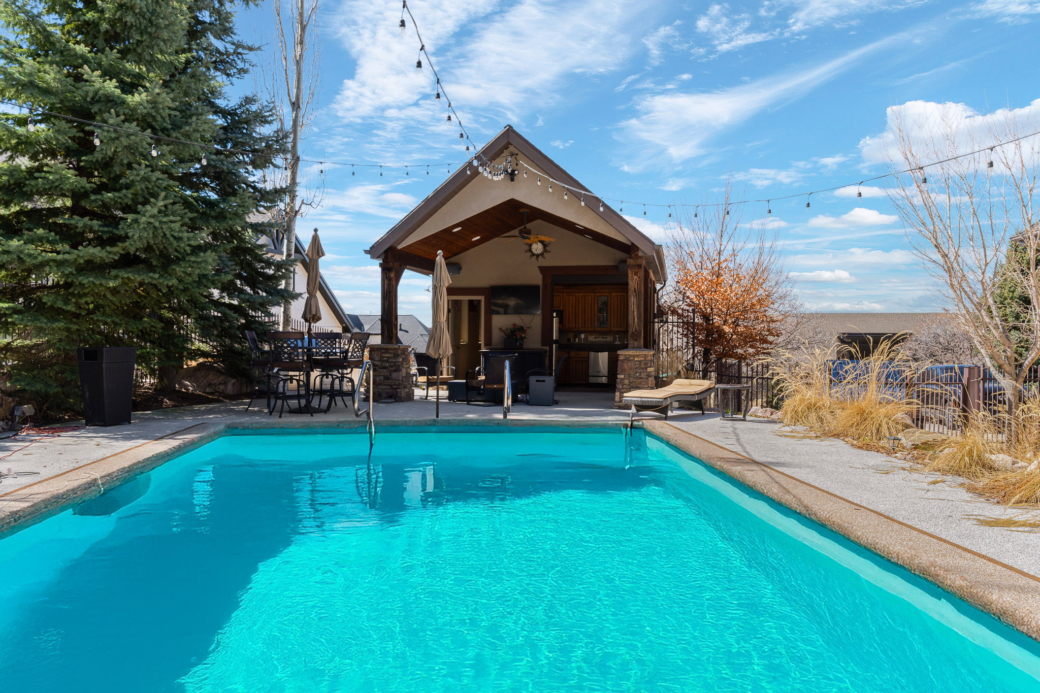 Expansive outdoor swimming pool with a surrounding concrete deck and integrated pool house featuring an open-air covered patio and built-in amenities