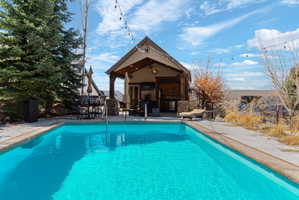 Expansive outdoor swimming pool with a surrounding concrete deck and integrated pool house featuring an open-air covered patio and built-in amenities
