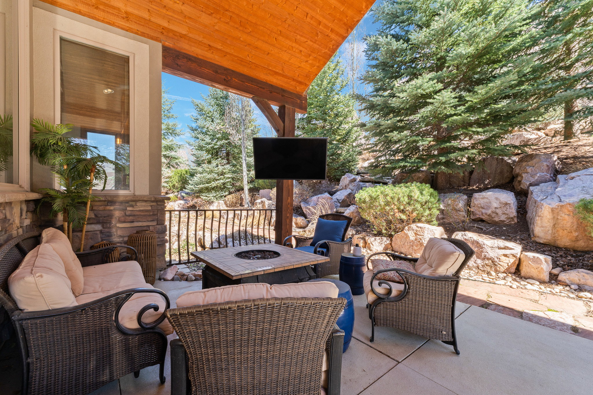 Covered patio featuring a wood-finish ceiling, stone columns, concrete flooring, and a built-in fire pit table