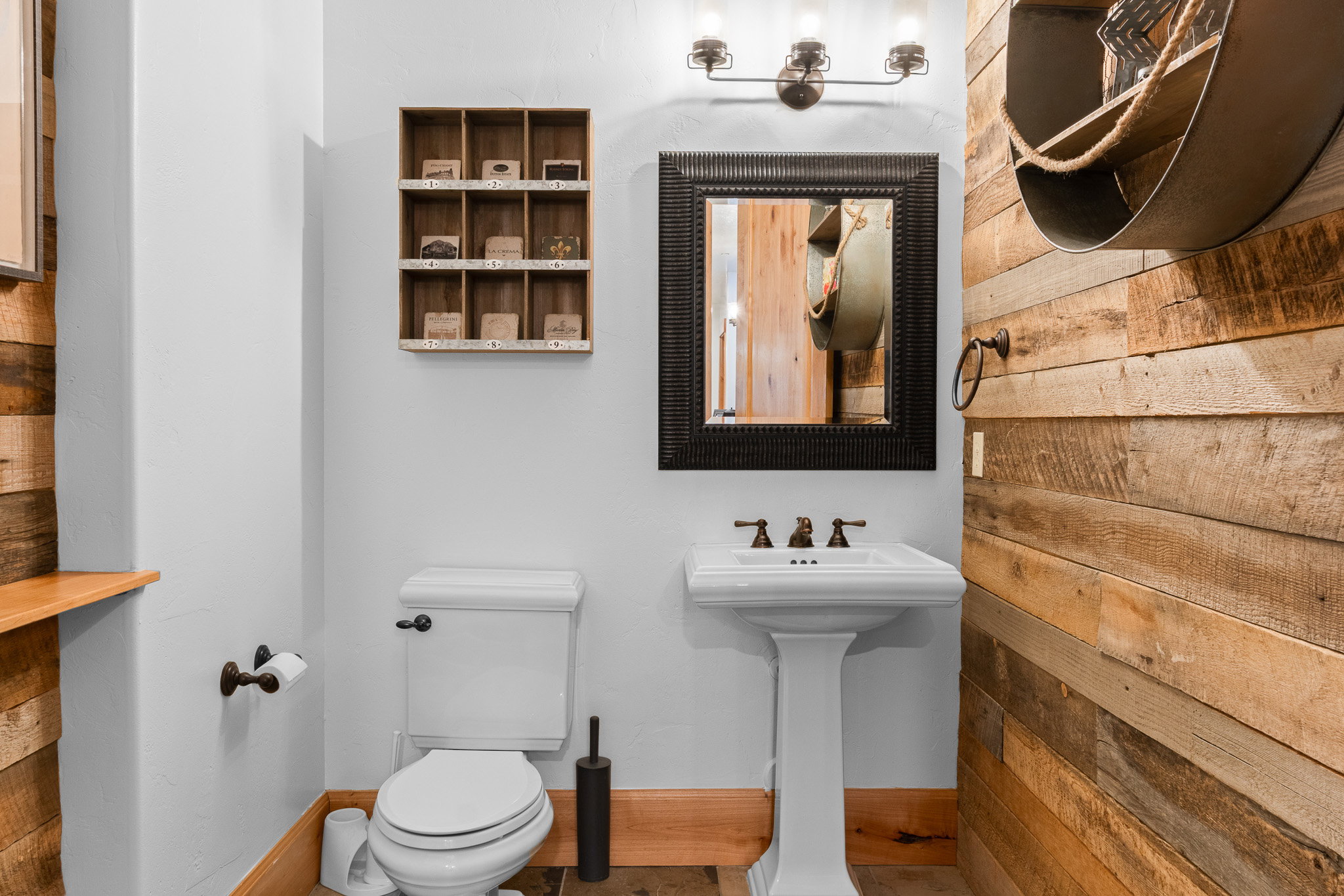 Powder room featuring a pedestal sink with bronze-finish faucet, a rectangular framed mirror, and a wood plank accent wall
