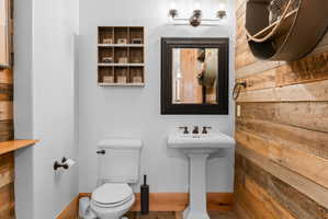 Powder room featuring a pedestal sink with bronze-finish faucet, a rectangular framed mirror, and a wood plank accent wall