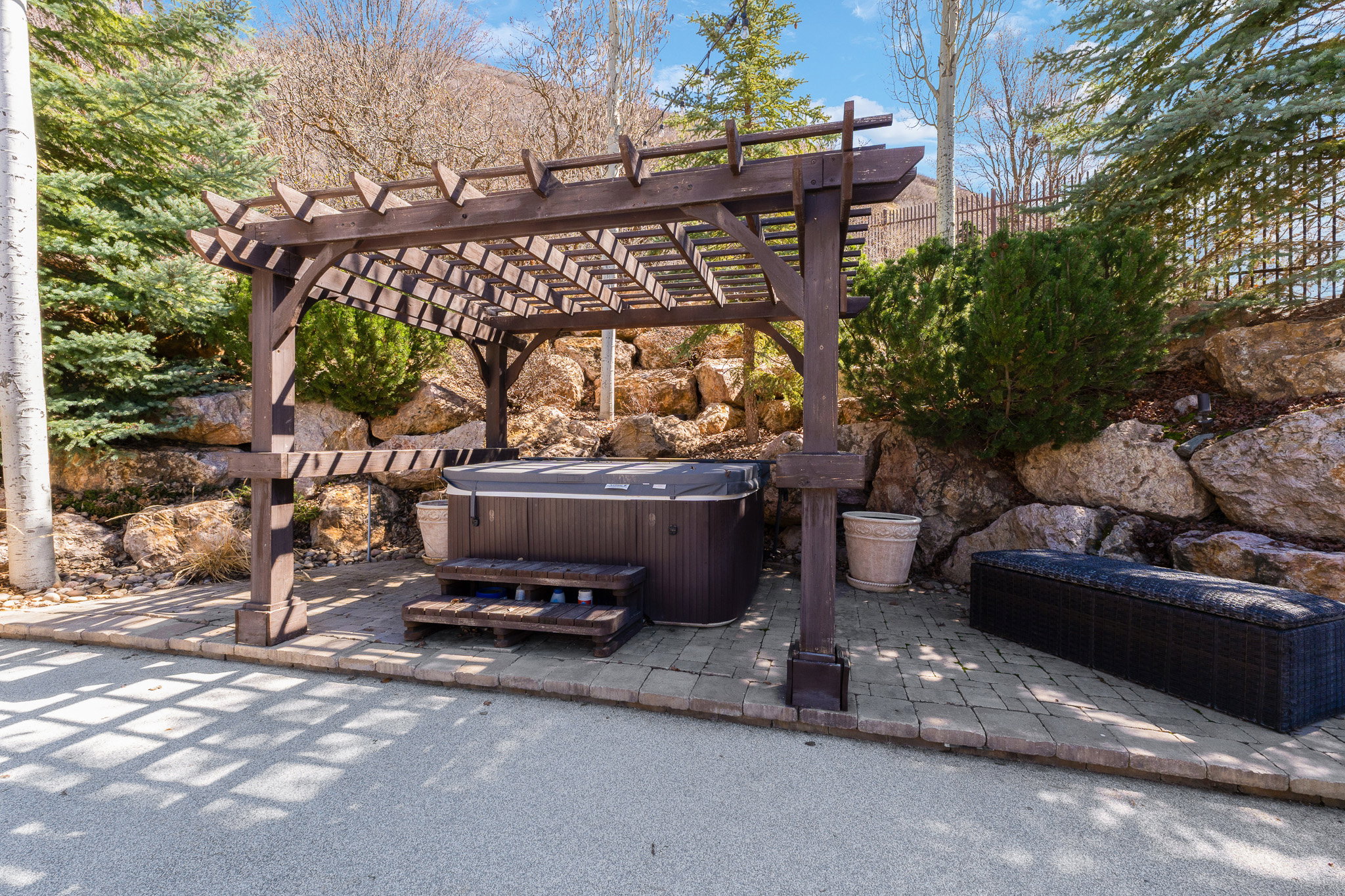 Outdoor spa area featuring a dark wood pergola, integrated hot tub, and stone paving