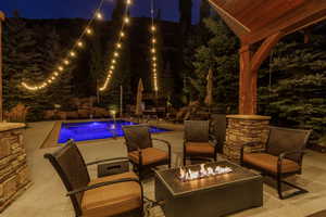 Outdoor entertainment area featuring a rectangular pool, stone-clad columns, a wood-beam pergola, and a built-in fire pit