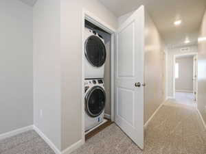 Dedicated laundry closet featuring a stackable washer and dryer, finished with white baseboards and neutral carpeting