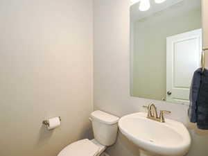 Powder room featuring a pedestal sink, brushed nickel faucet, mirror, and a white toilet