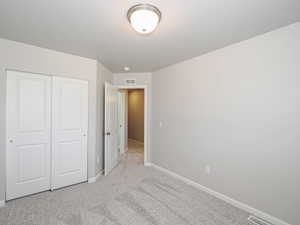 Bedroom featuring light gray wall paint, gray textured carpeting, a flush-mount ceiling light fixture, and white bi-fold closet doors