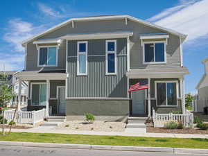 Modern duplex exterior featuring a combination of horizontal and vertical siding, concrete foundation, covered entryways, white picket fencing, and a manicured lawn