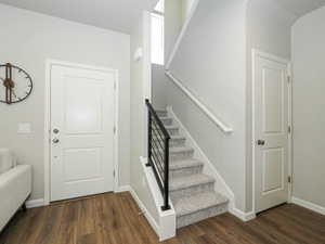 Entryway featuring wood-finish flooring, a white paneled entry door with chrome hardware, and a staircase with textured carpet treads and a contemporary black metal railing