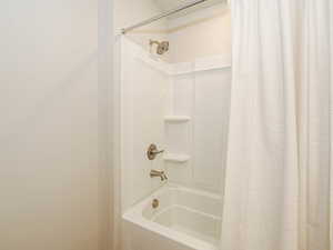 Bathtub and shower combination featuring a brushed nickel showerhead, matching faucet, and two integrated corner shelves