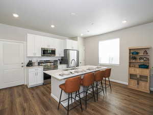 Open-concept kitchen featuring white cabinetry, stainless steel appliances, and wood-finish flooring