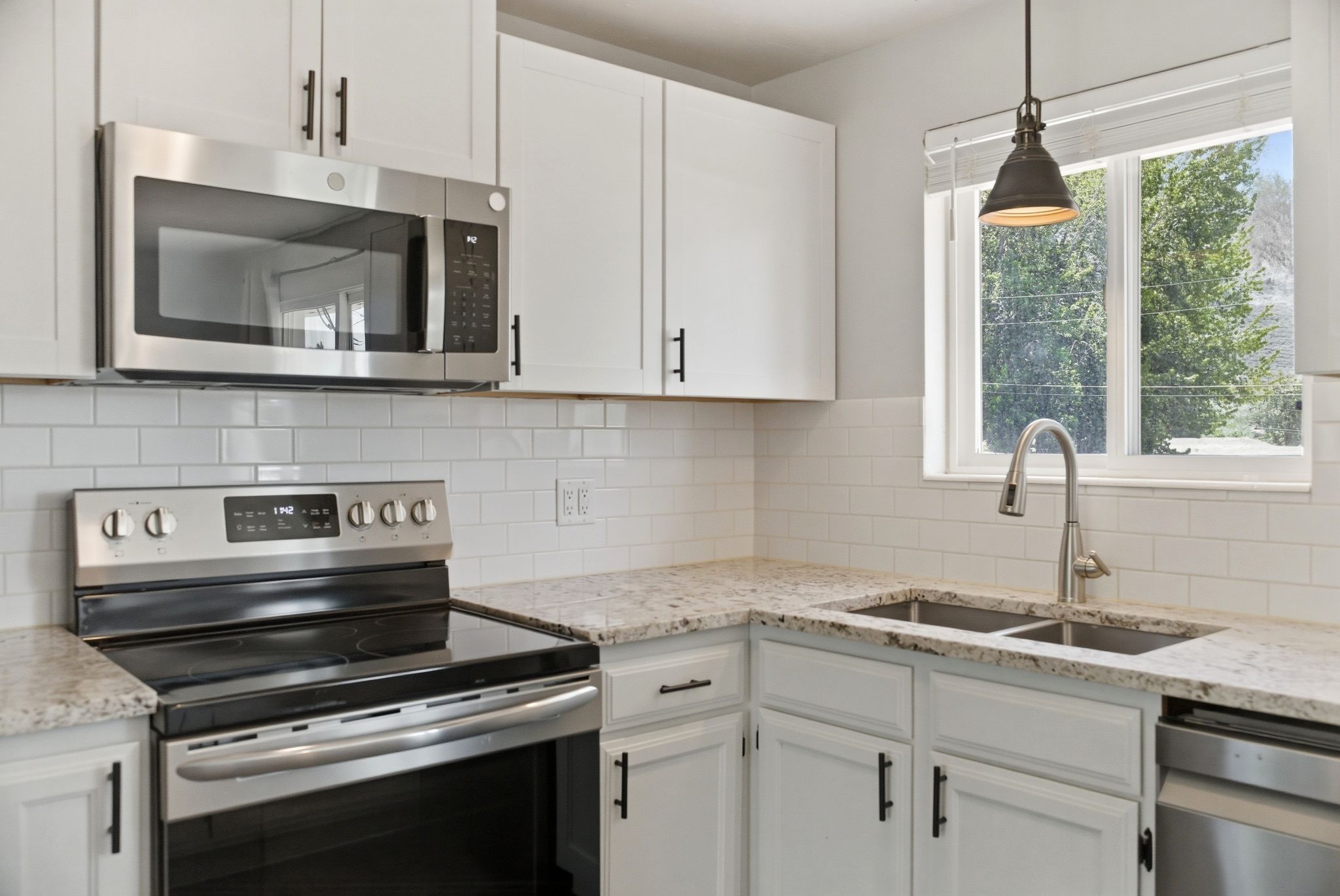 Kitchen featuring white cabinetry, subway tile backsplash, stainless steel appliances, granite countertops, and a dual-basin sink with a pull-down faucet