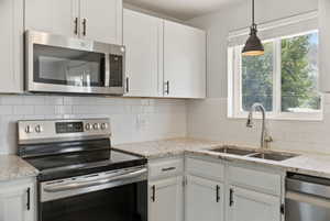 Kitchen featuring white cabinetry, subway tile backsplash, stainless steel appliances, granite countertops, and a dual-basin sink with a pull-down faucet
