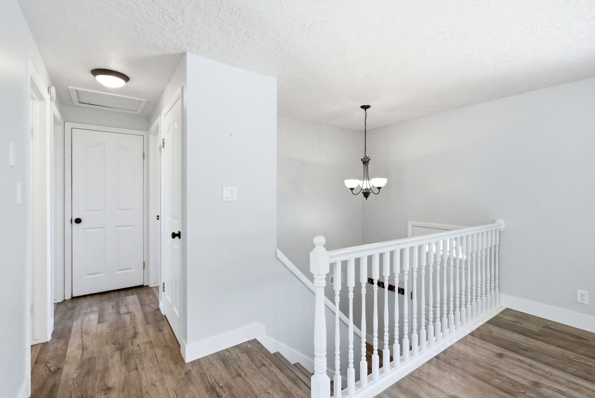 Upper-level hallway featuring wood-finish flooring, white panel doors, a white baluster railing, and a bronze-finish chandelier