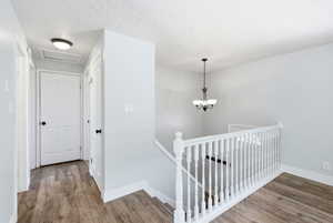 Upper-level hallway featuring wood-finish flooring, white panel doors, a white baluster railing, and a bronze-finish chandelier