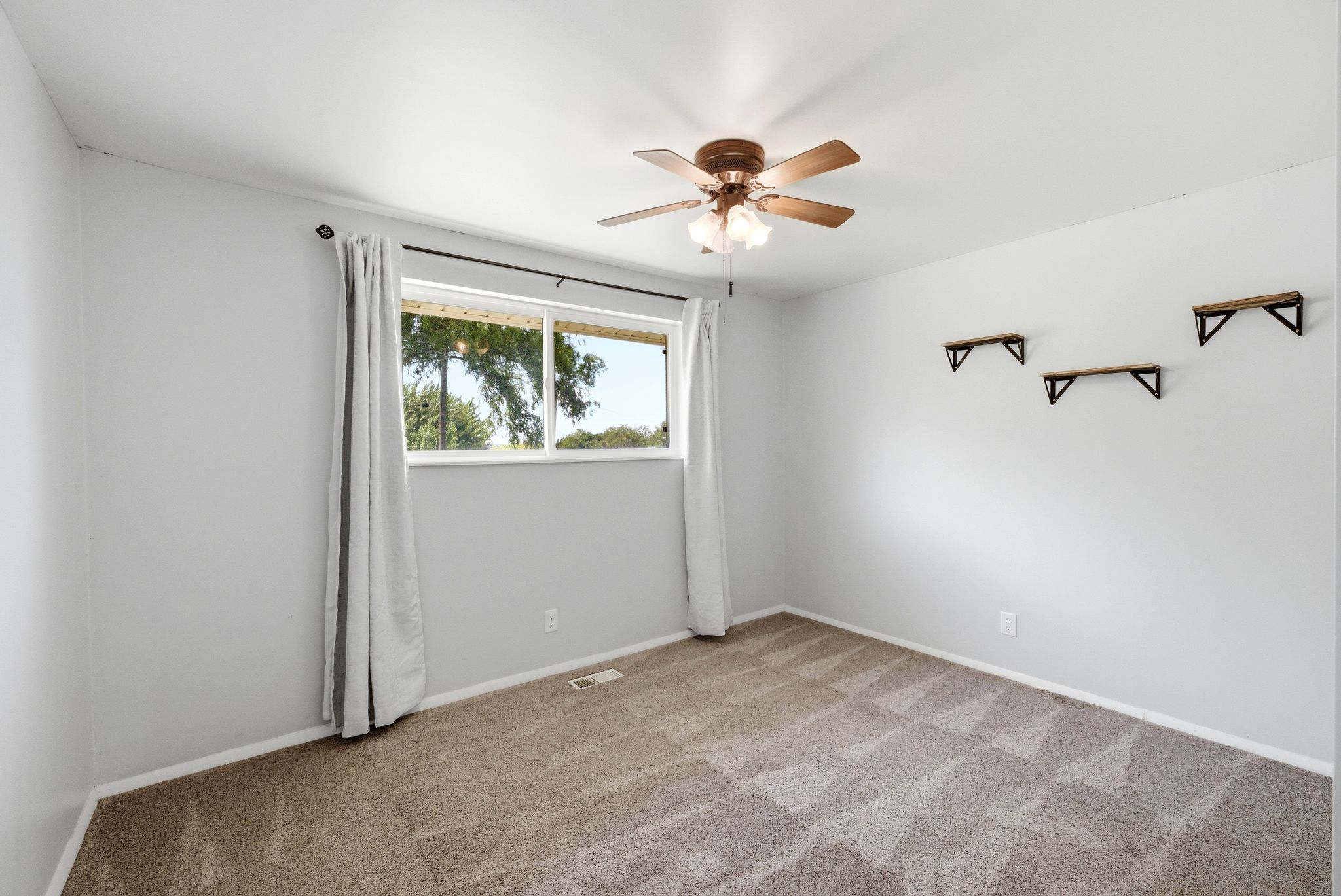 Carpeted room featuring a ceiling fan with integrated lighting, a large window, and three wall-mounted shelves