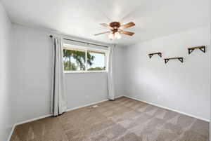 Carpeted room featuring a ceiling fan with integrated lighting, a large window, and three wall-mounted shelves