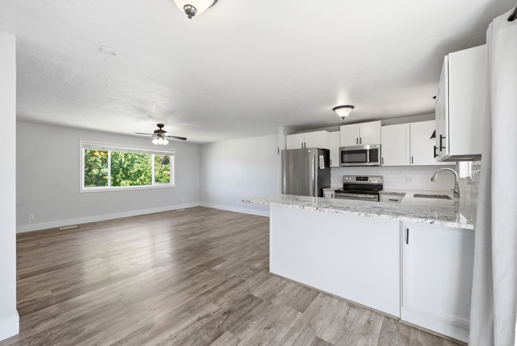 Open-concept living space featuring wood-finish flooring, a contemporary ceiling fan, and a large window