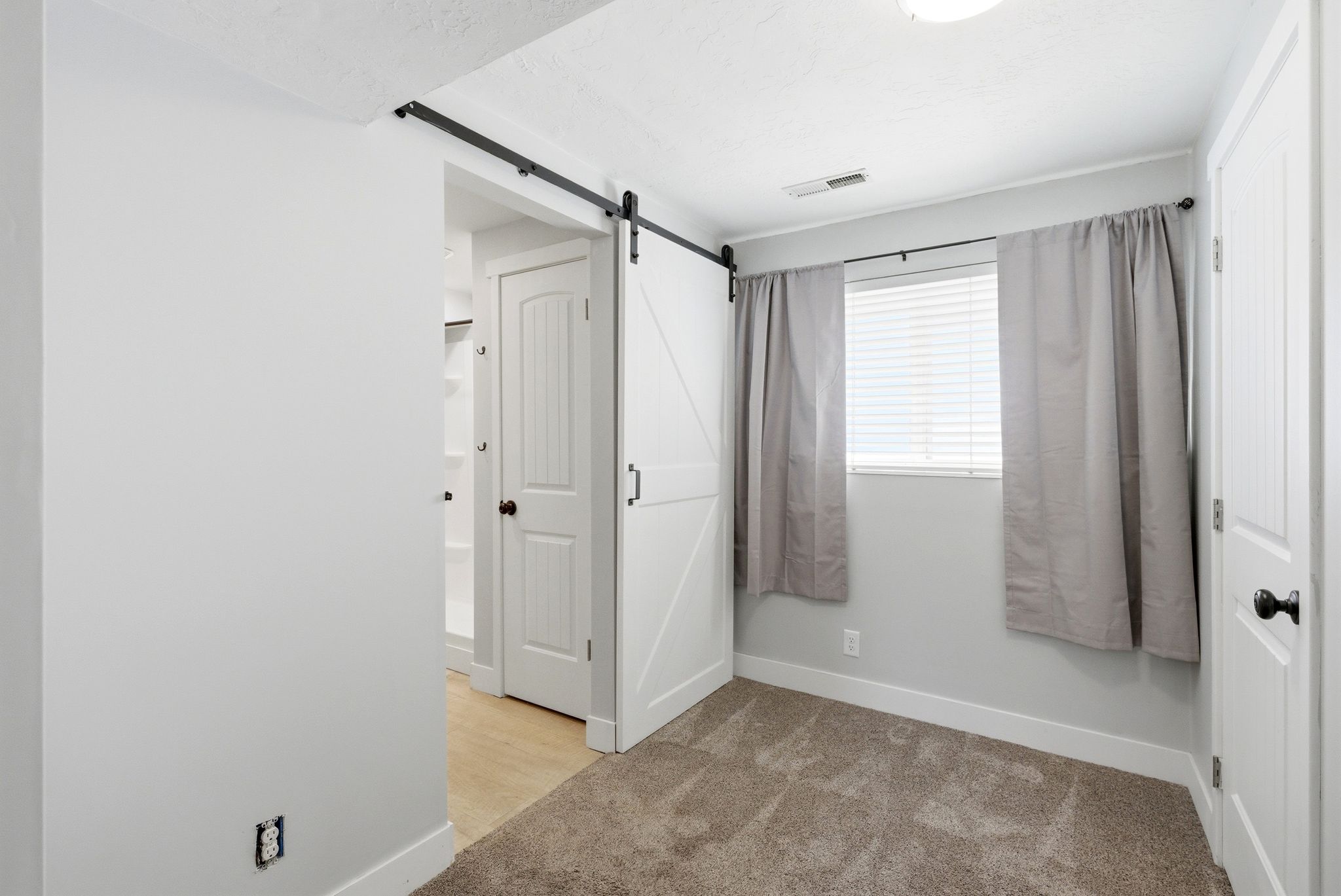 Interior room featuring neutral-toned walls, carpet flooring, and a white barn door on a black rail system