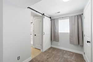 Interior room featuring neutral-toned walls, carpet flooring, and a white barn door on a black rail system
