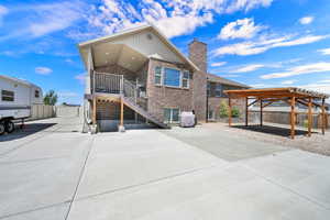 Brick exterior with a covered deck, exterior staircase, a concrete patio, and a wood pergola over a gravel area