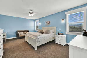 Carpeted room featuring a ceiling fan with integrated lighting, two windows with blinds, and wall-mounted sconce lighting