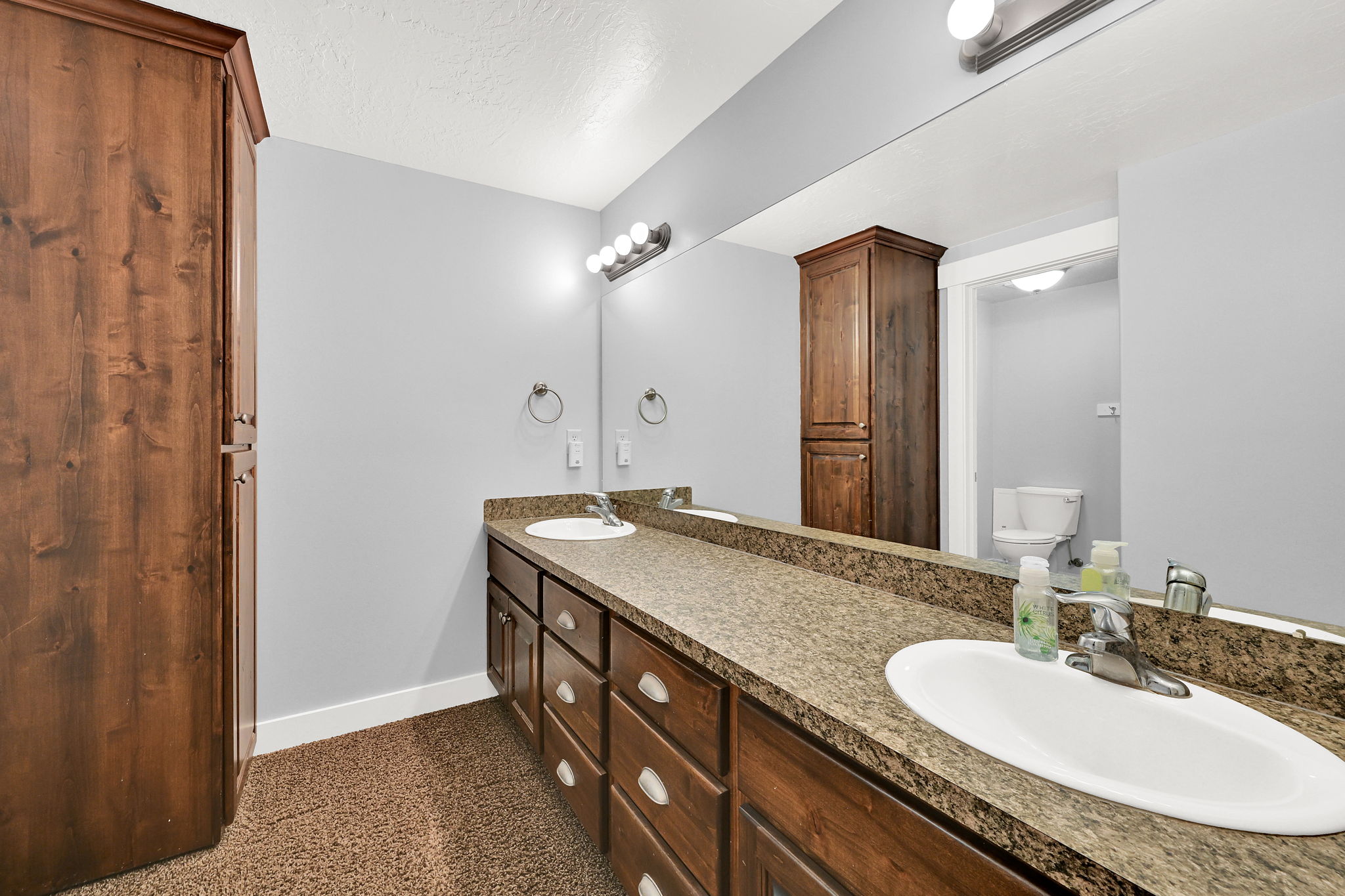 Bathroom featuring dual under-mount sinks with chrome fixtures, a long vanity with wood-finish cabinetry, and a full-width mirror