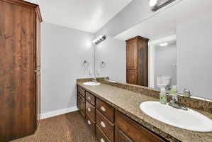 Bathroom featuring dual under-mount sinks with chrome fixtures, a long vanity with wood-finish cabinetry, and a full-width mirror