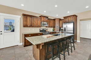 Kitchen featuring wood-finish cabinetry, granite countertops, stainless steel appliances, and tile flooring