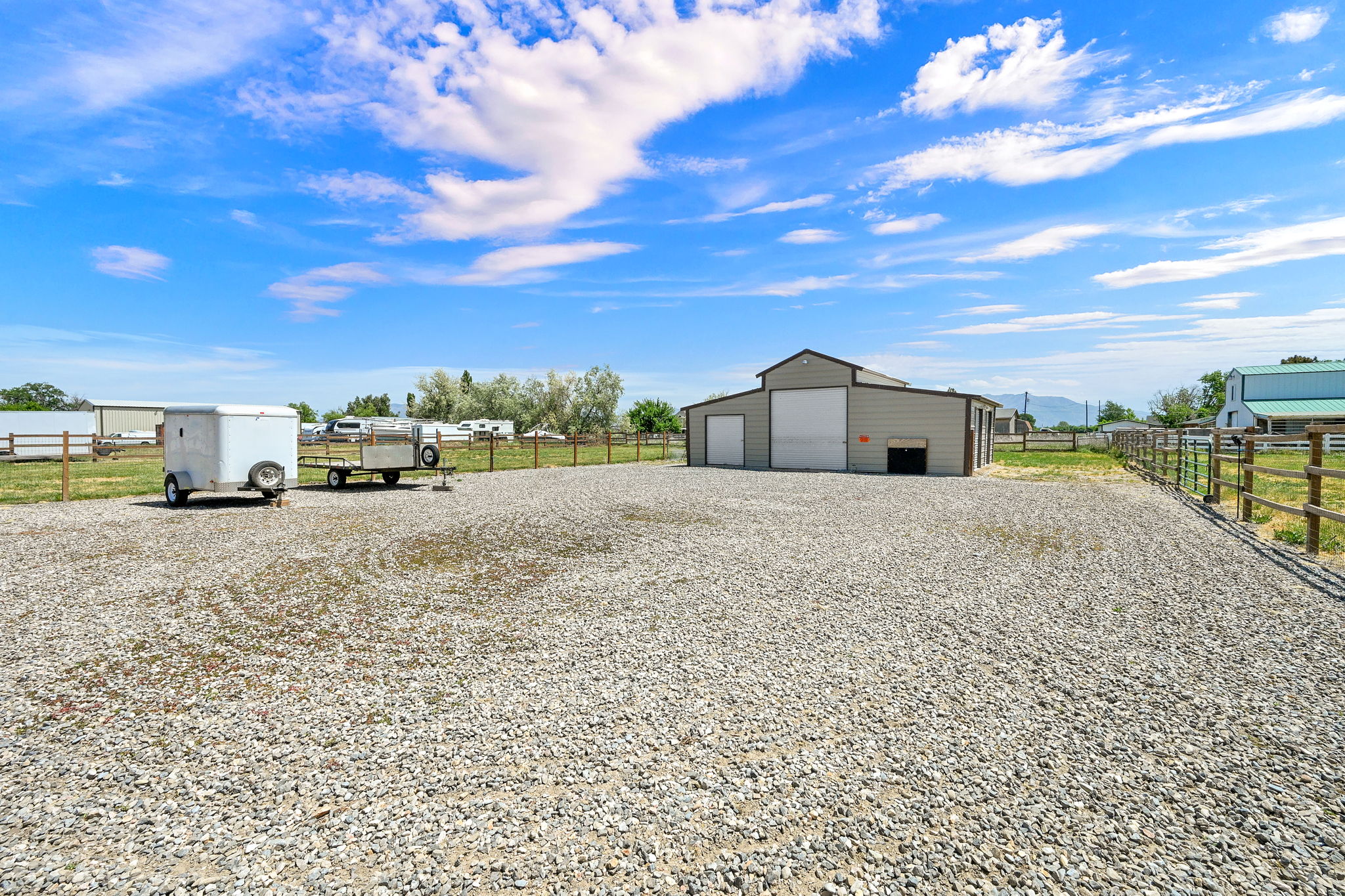 Expansive gravel lot featuring a large outbuilding with multiple garage doors and a separate entry