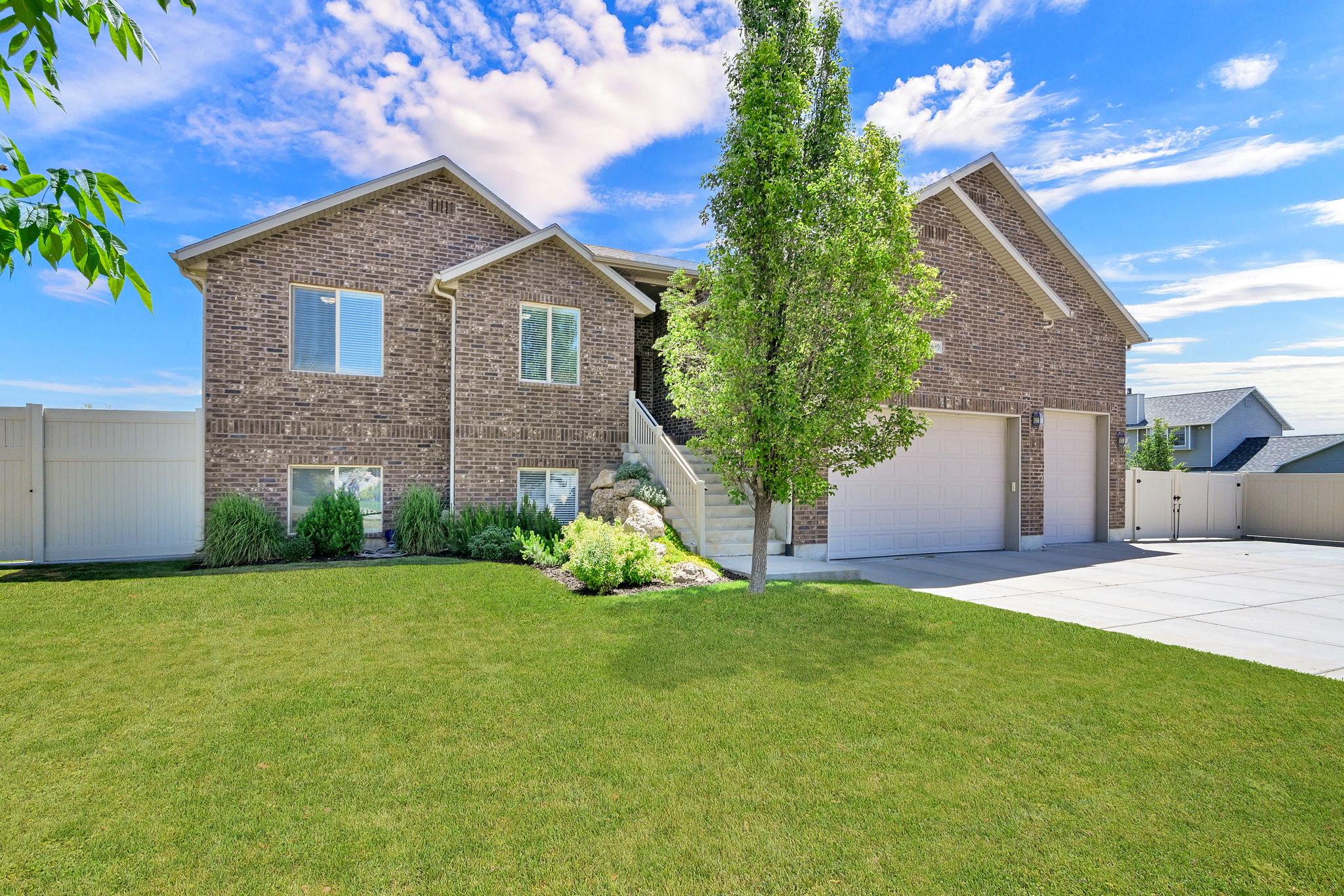 Brick exterior residence featuring a green lawn, established landscaping, and a multi-level concrete driveway