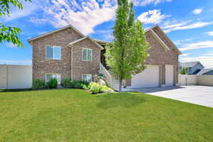 Brick exterior residence featuring a green lawn, established landscaping, and a multi-level concrete driveway