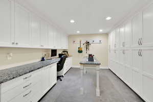 Dedicated functional room featuring extensive white cabinetry, recessed lighting, a stone-finish countertop workspace, and carpeted flooring